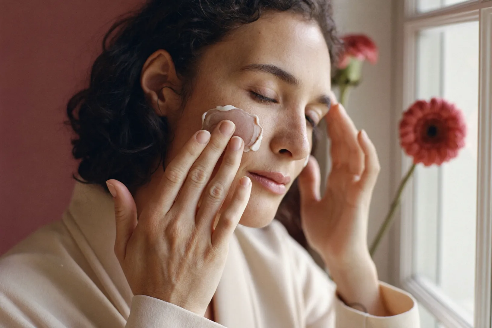 A woman gently pressing moisturizer into her cheek in soft morning light