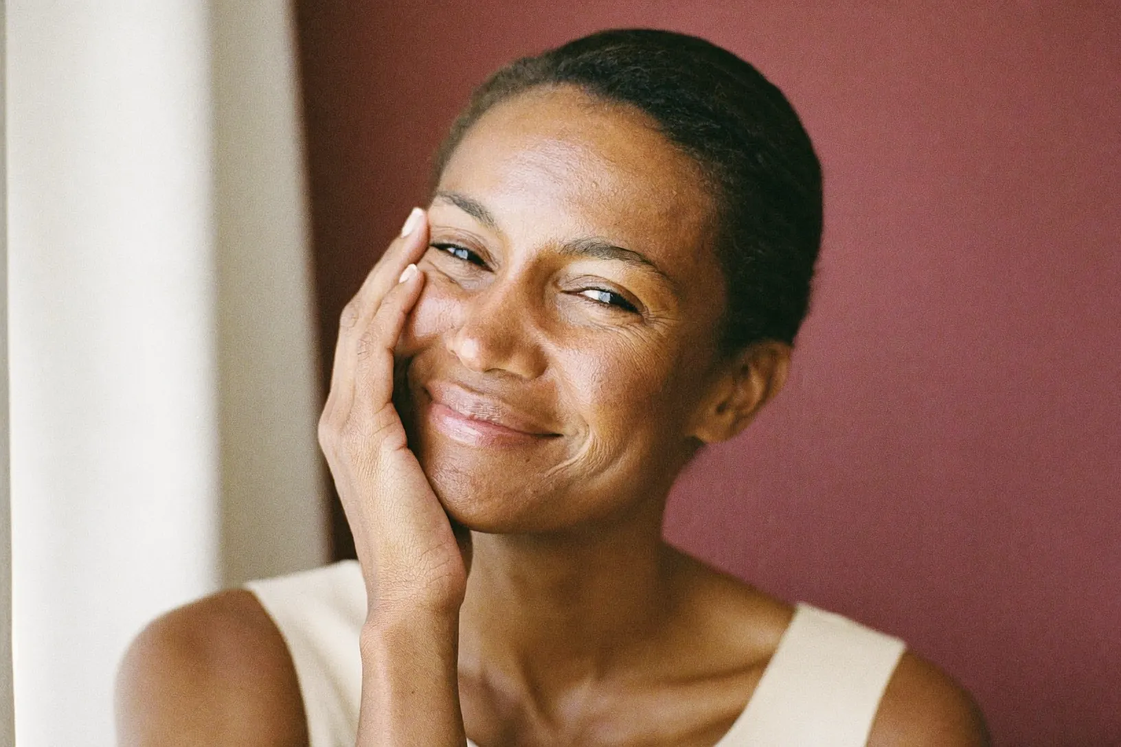 A woman smiling calmly with a hand resting on her cheek in warm light